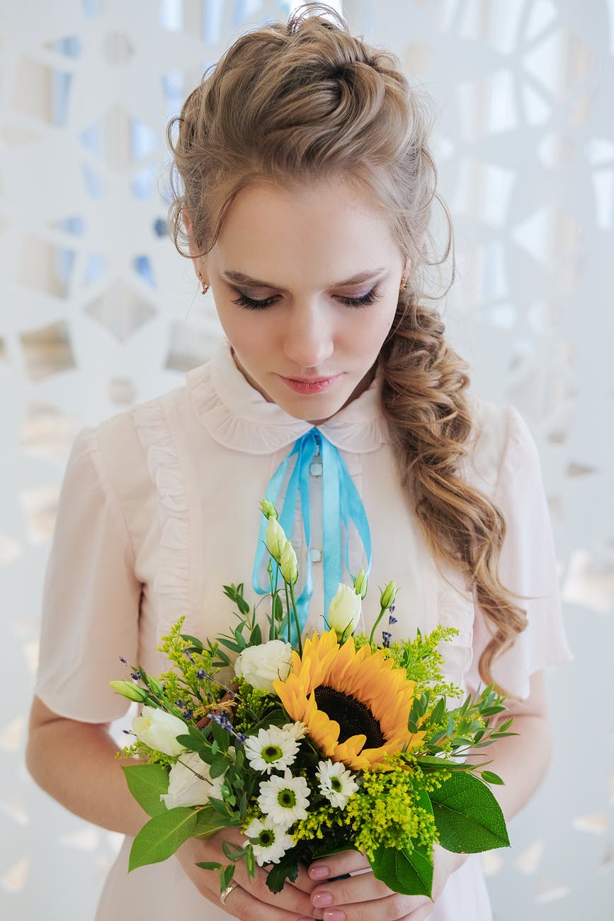 feminine young woman with bouquet of fresh flowers standing in light room
