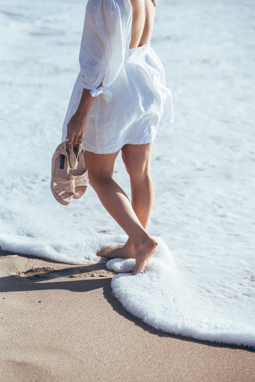 barefoot woman in white clothes walking in foamy sea