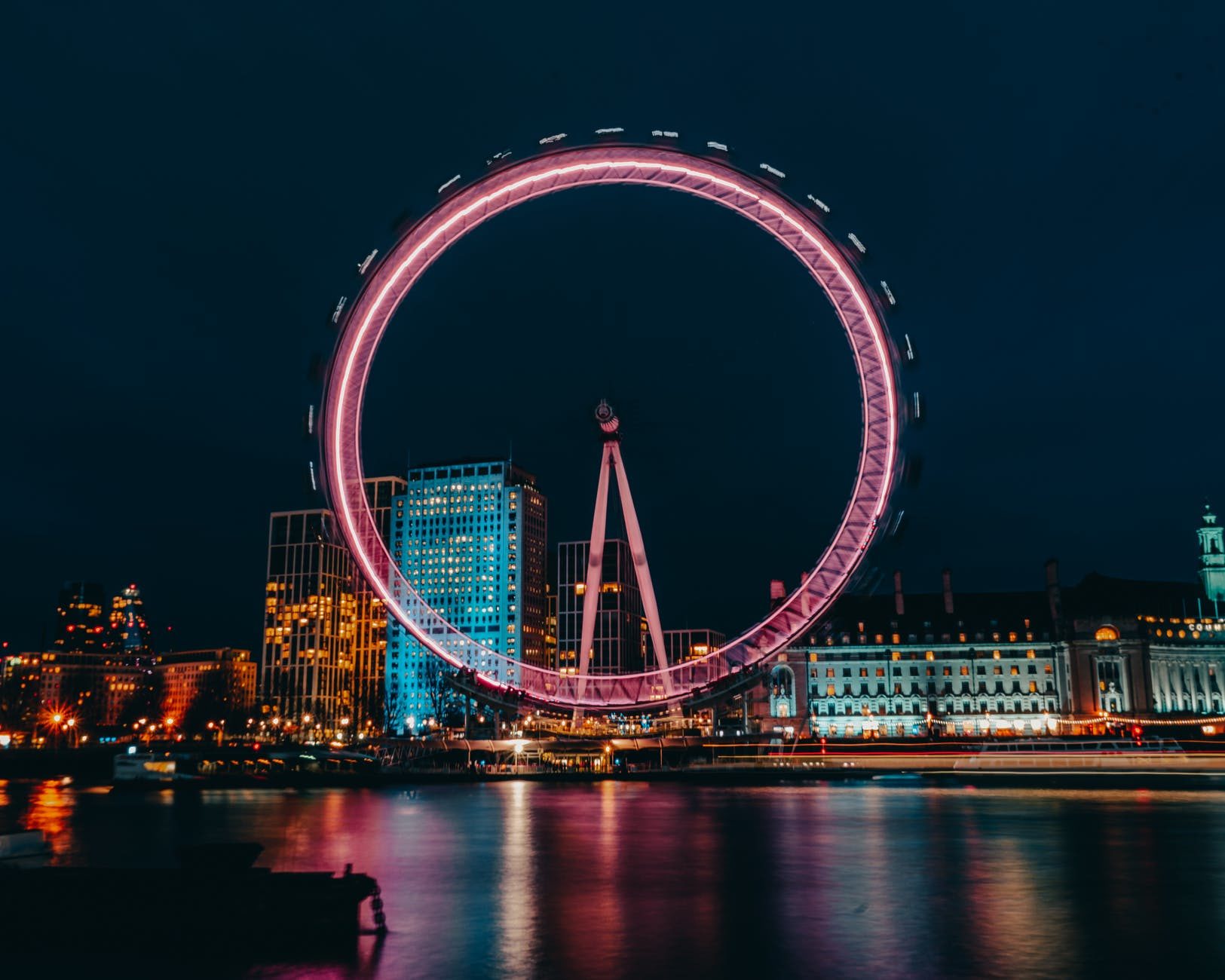 luminous ferris wheel in modern city district on river bank at night