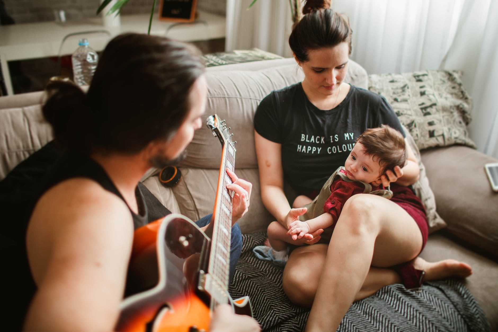 father playing guitar for mother with baby