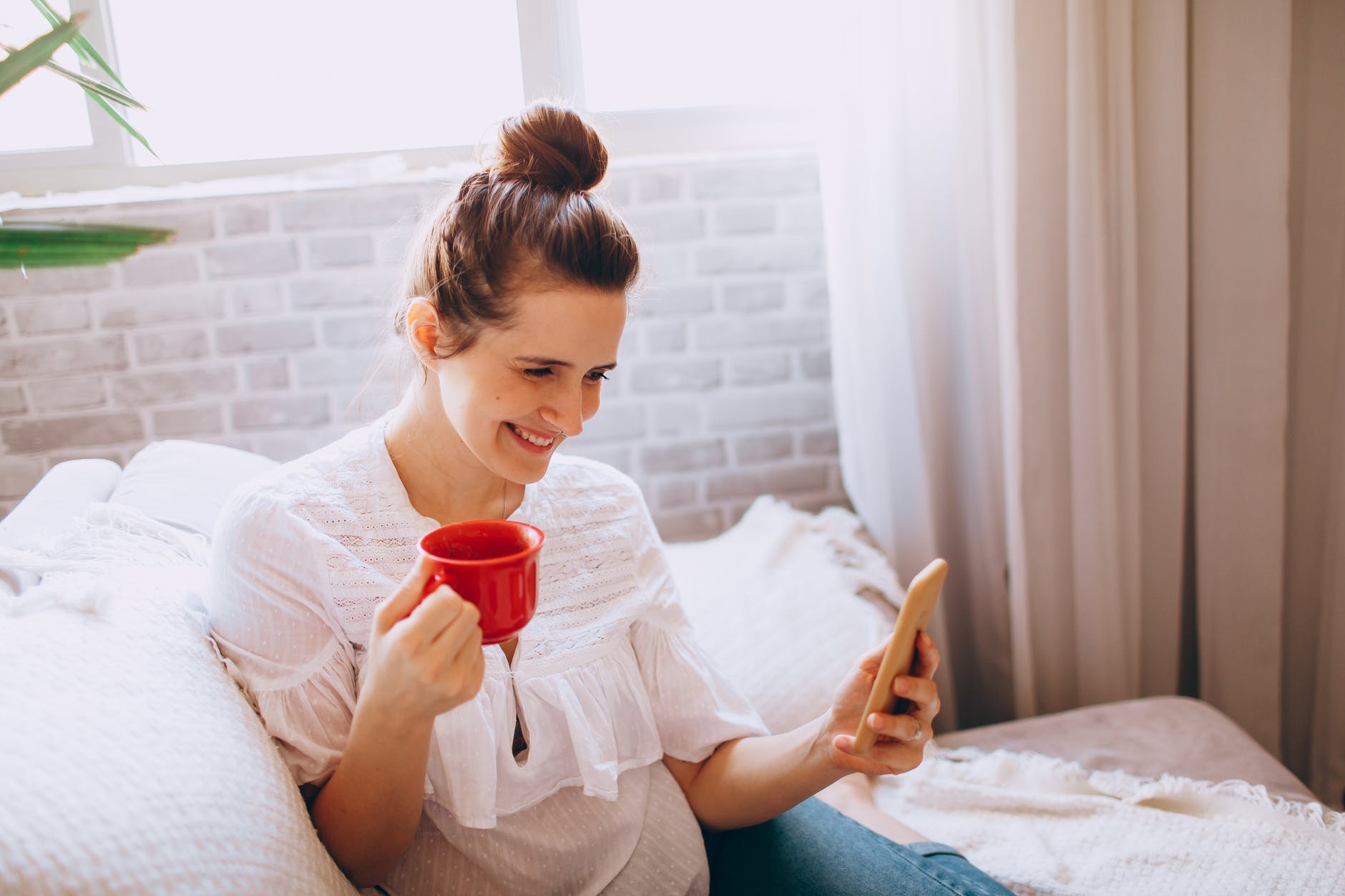 smiling woman with cup of coffee using smartphone