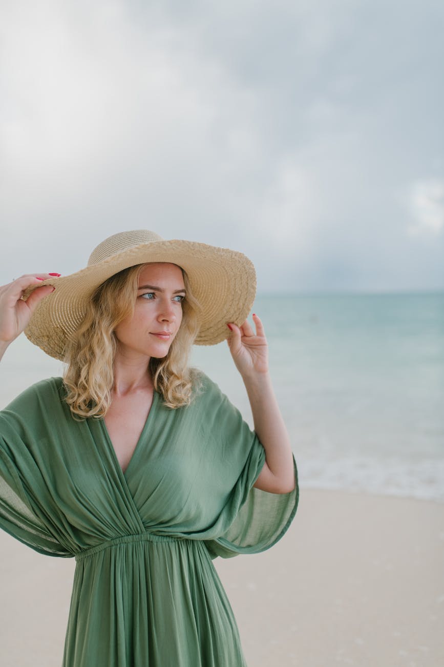 tranquil woman in straw hat on sandy beach near sea