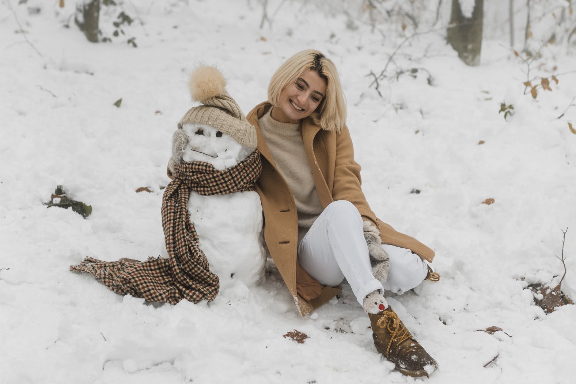 happy woman sitting on snow covered beside the snowman