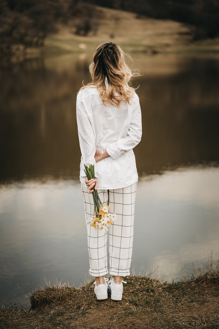 unrecognizable trendy woman with blooming daffodils contemplating river from shore